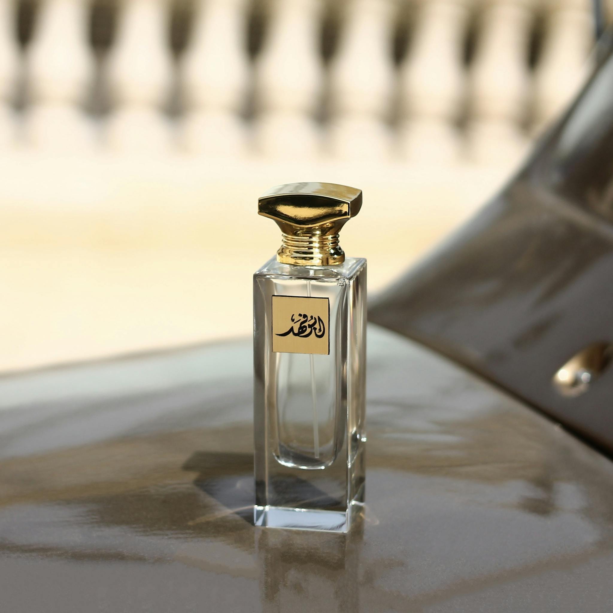 A luxurious perfume bottle with a gold cap and Arabic script against a blurred backdrop.