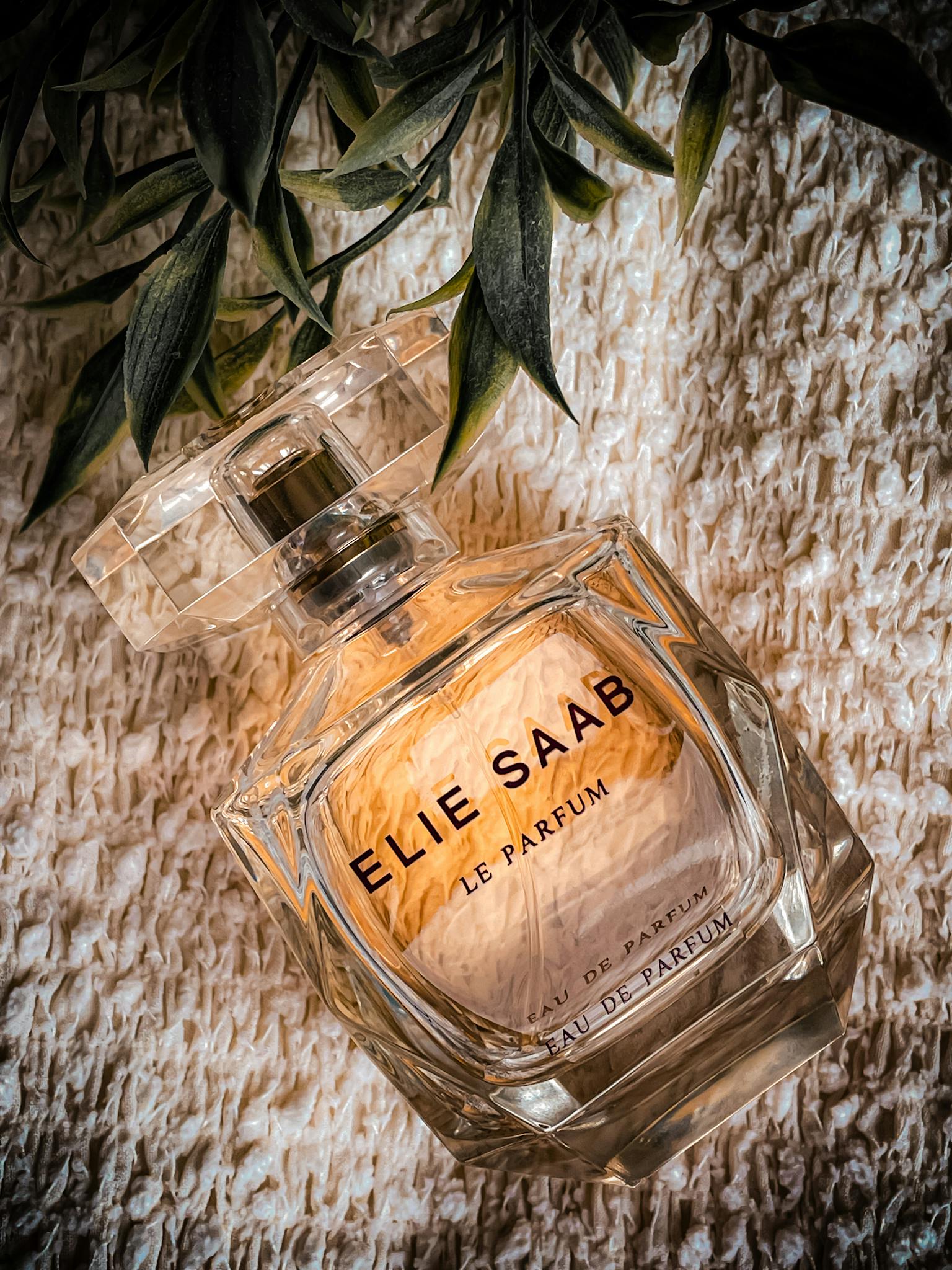 Luxurious Elie Saab perfume bottle with a botanical accent on textured fabric.